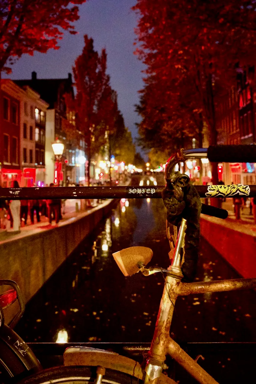 front detail of a bicycle leaning against the railings across a canal in Amsterdam tinted in red lights